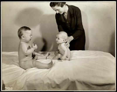 Two babies sitting up in bed, one being supported by a nurse, the other holding a toy car and crying at the Maternity Center Association at 70th Street East River, New York, 1935 by Byron Company